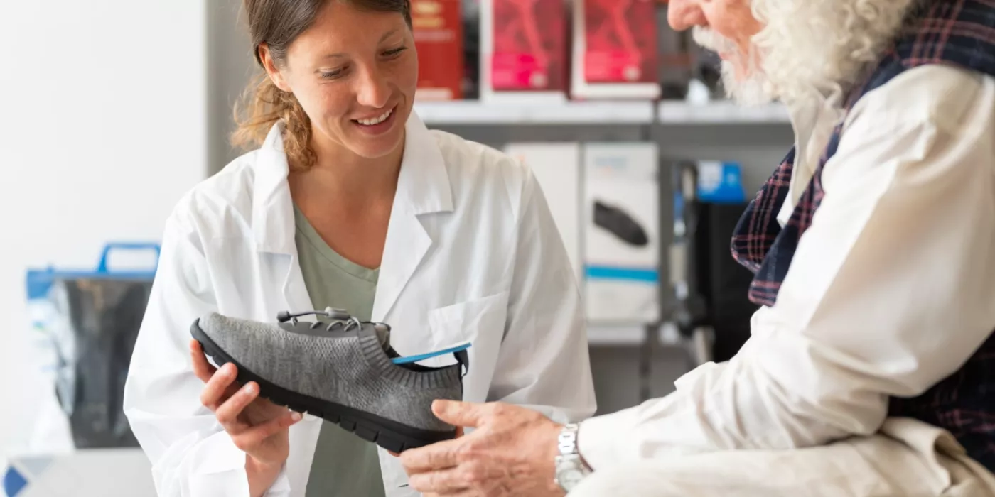 Mitarbeiterin im Sanitätshaus berät älteren Mann zu orthopädischen Schuheinlagen